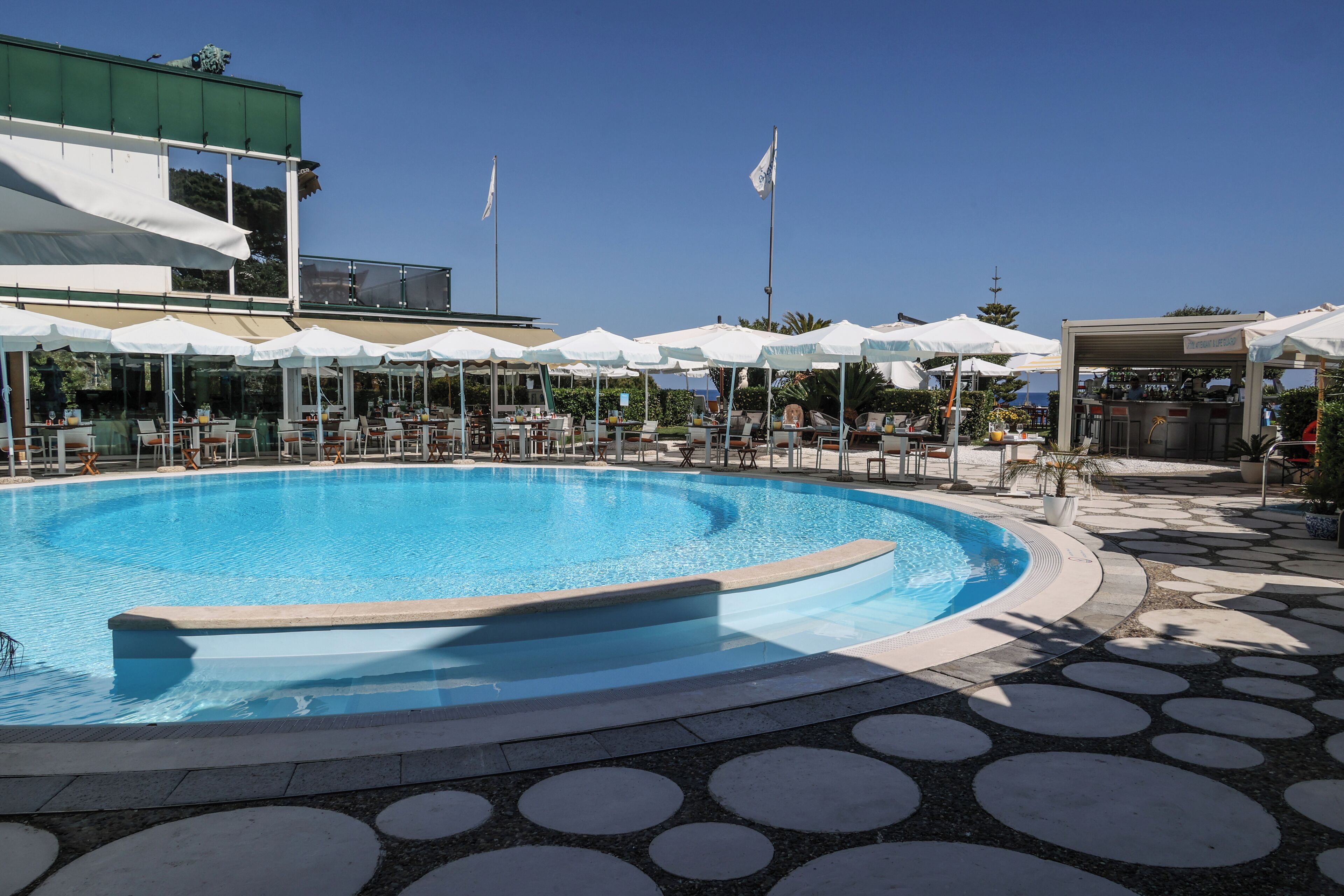 Area piscina con lettini e ombrelloni, circondata da un percorso pedonale decorato.