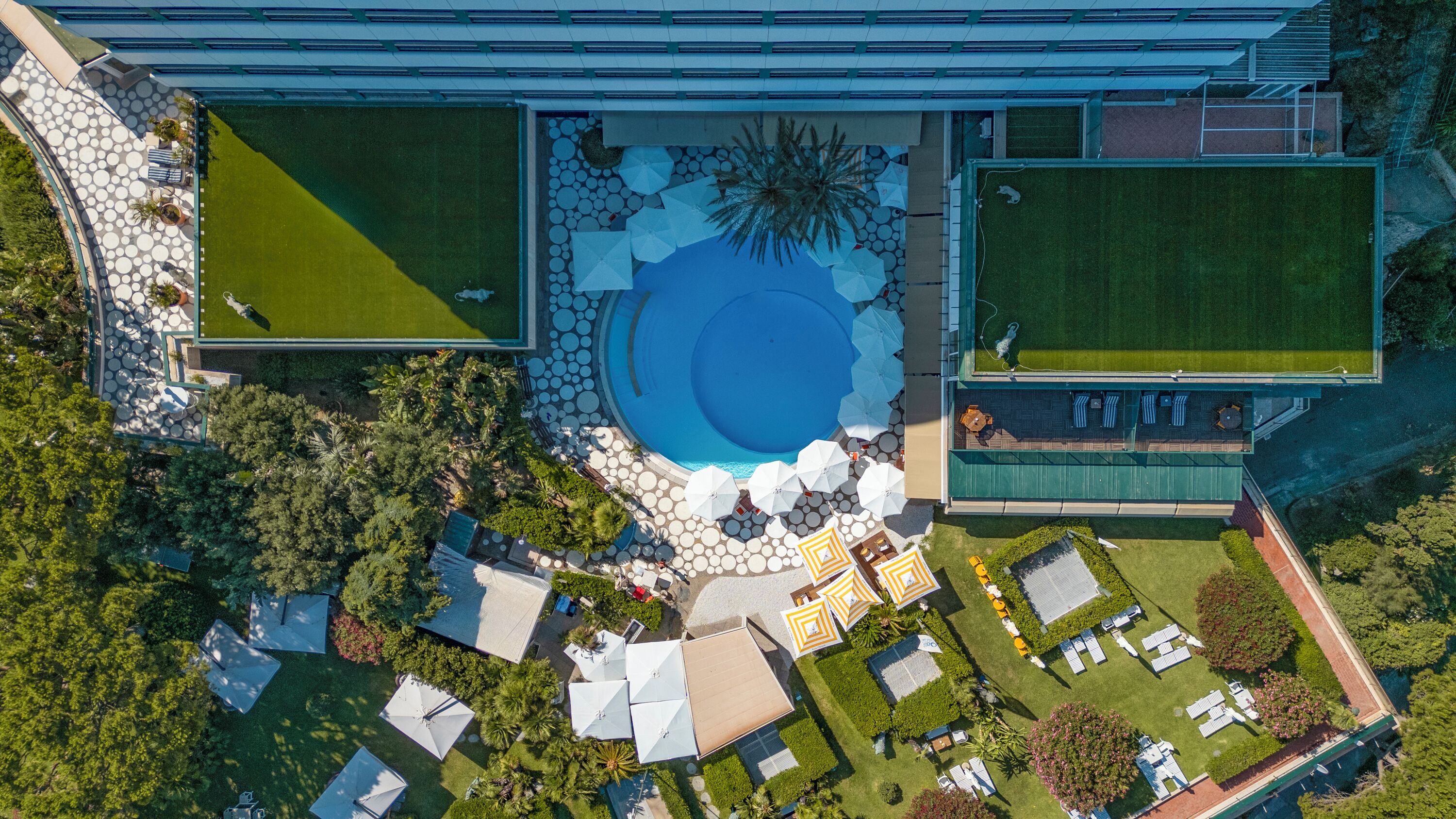 Ein Luftbild eines modernen Hotels mit einem zentralen Schwimmbad, Außenbereich-Sitzgelegenheiten und üppiger Bepflanzung.