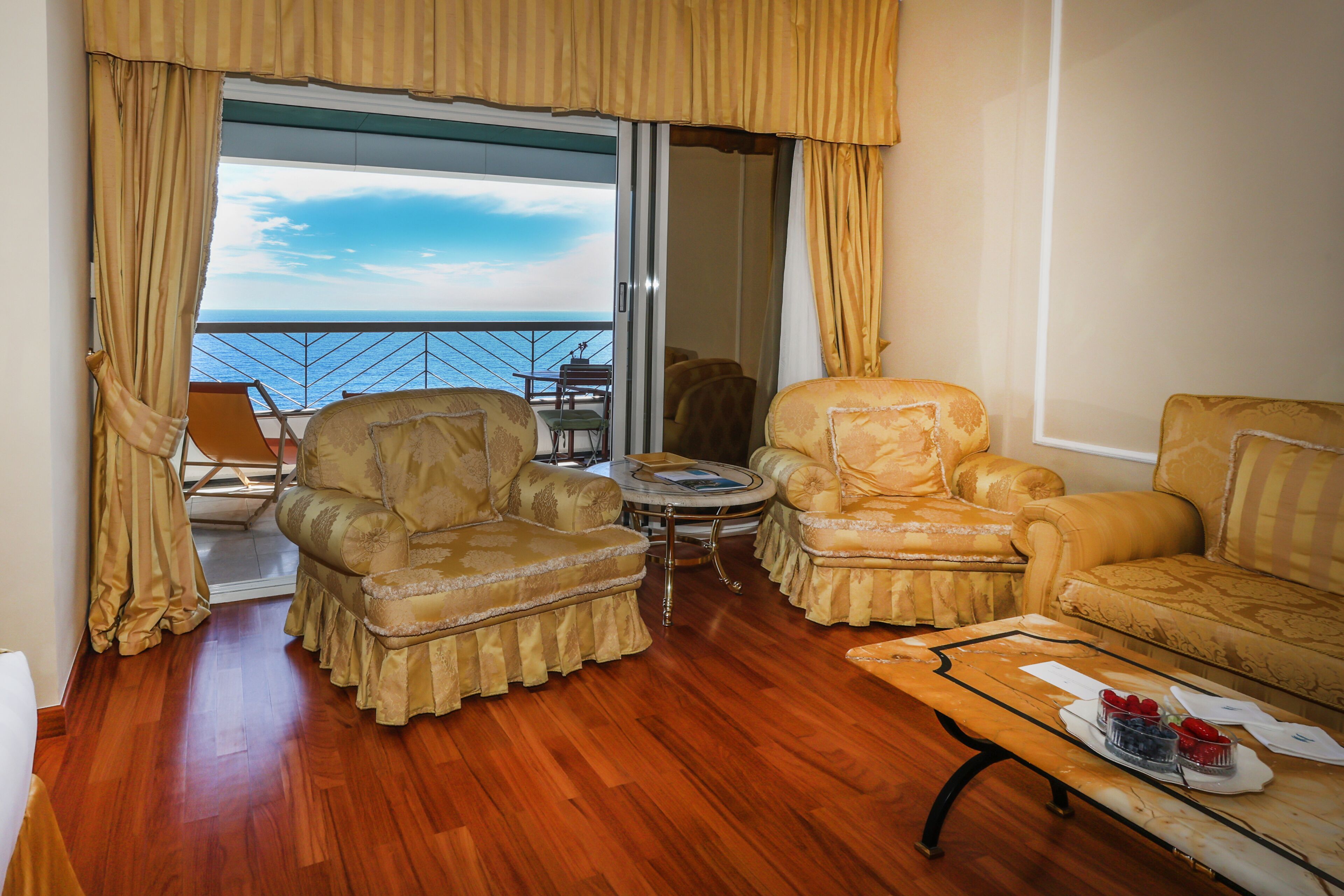 A balcony with two armchairs, a small round table, and a wooden coffee table with a tray of fruit.