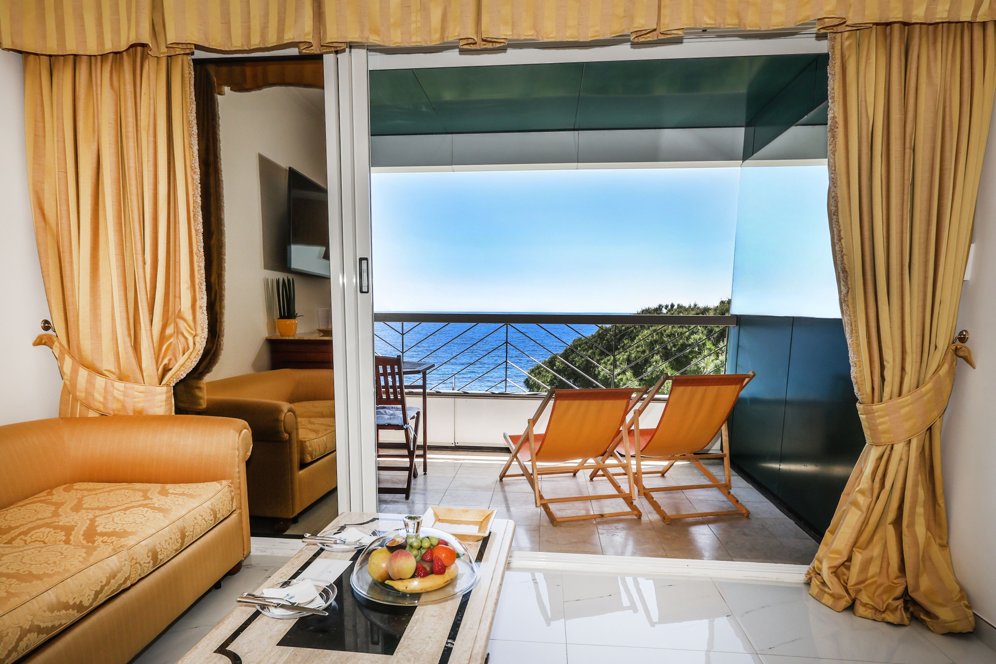 A balcony with a sofa, two chairs, a table with fruit, and a TV.