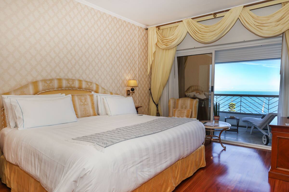 Ein Hotelzimmer mit einem großen Bett, einem kleinen Tisch, einem Stuhl und einem Balkon mit Blick.