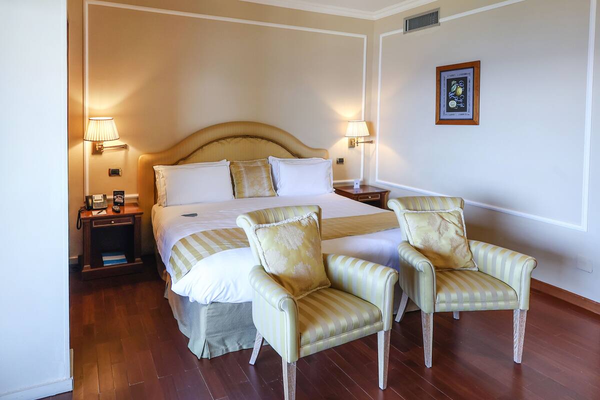 Ein Hotelzimmer mit einem großen Bett, zwei Nachttischlampen, einem Nachttisch, einem Sessel und einem gerahmten Bild an der Wand.