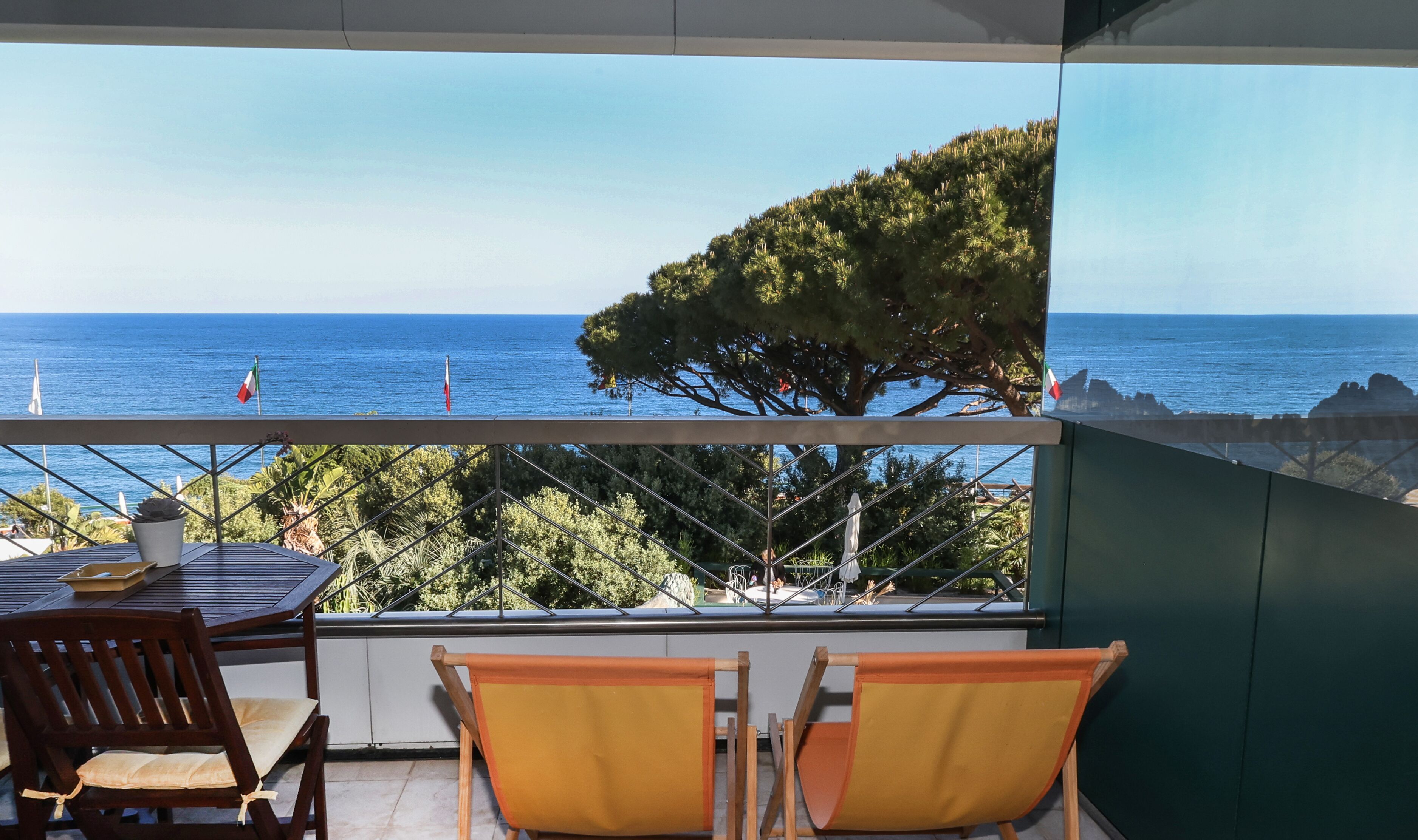 Un balcón con mesa y sillas, con vistas a la costa, árboles y el mar.