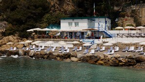 Un hôtel situé sur la côte, doté d’une piscine, de chaises longues et de parasols.