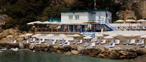 A coastal hotel with a pool area, sun loungers, and umbrellas.