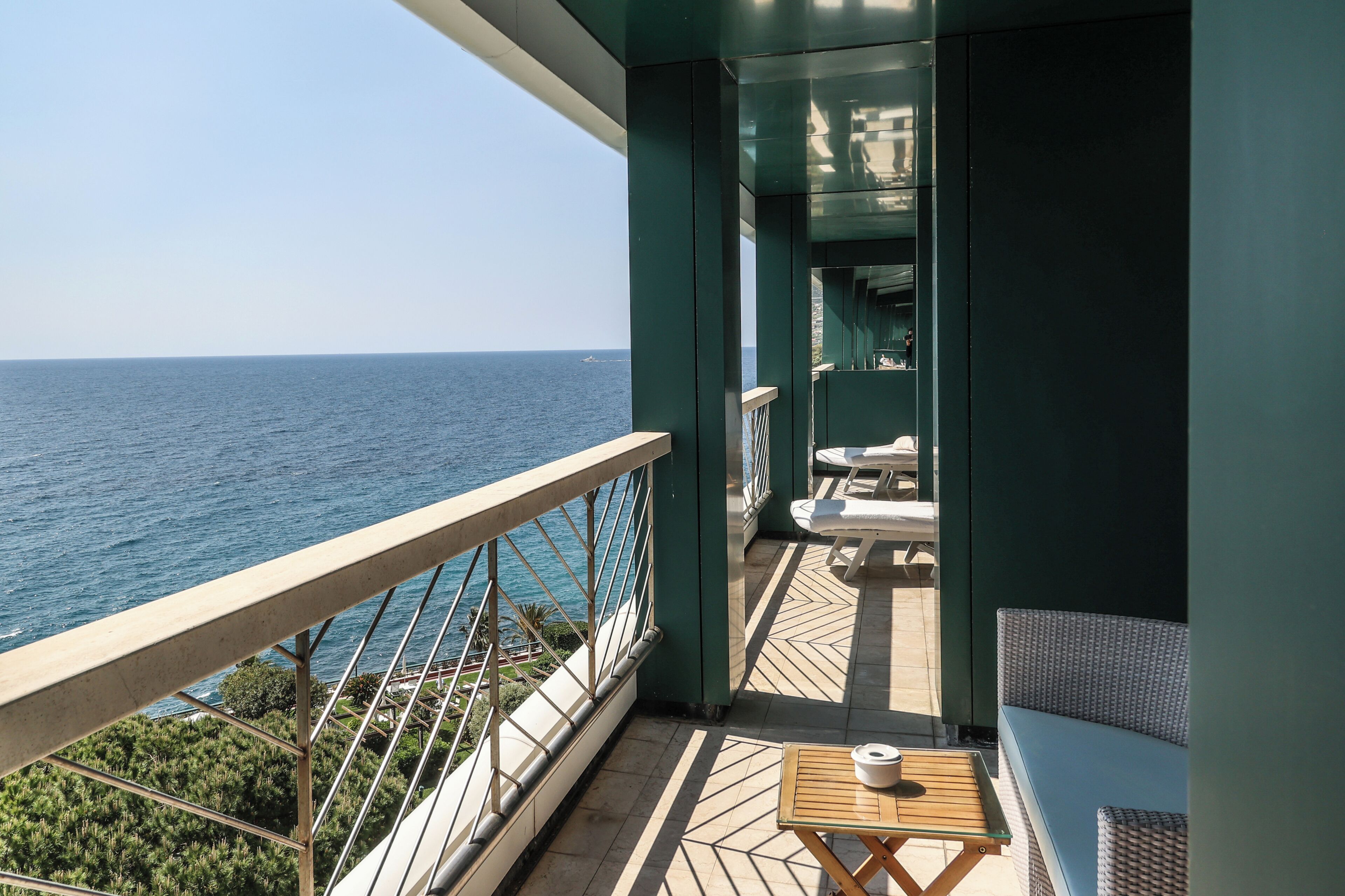 A balcony with a view of the sea, a small table with a cup, and a sofa.