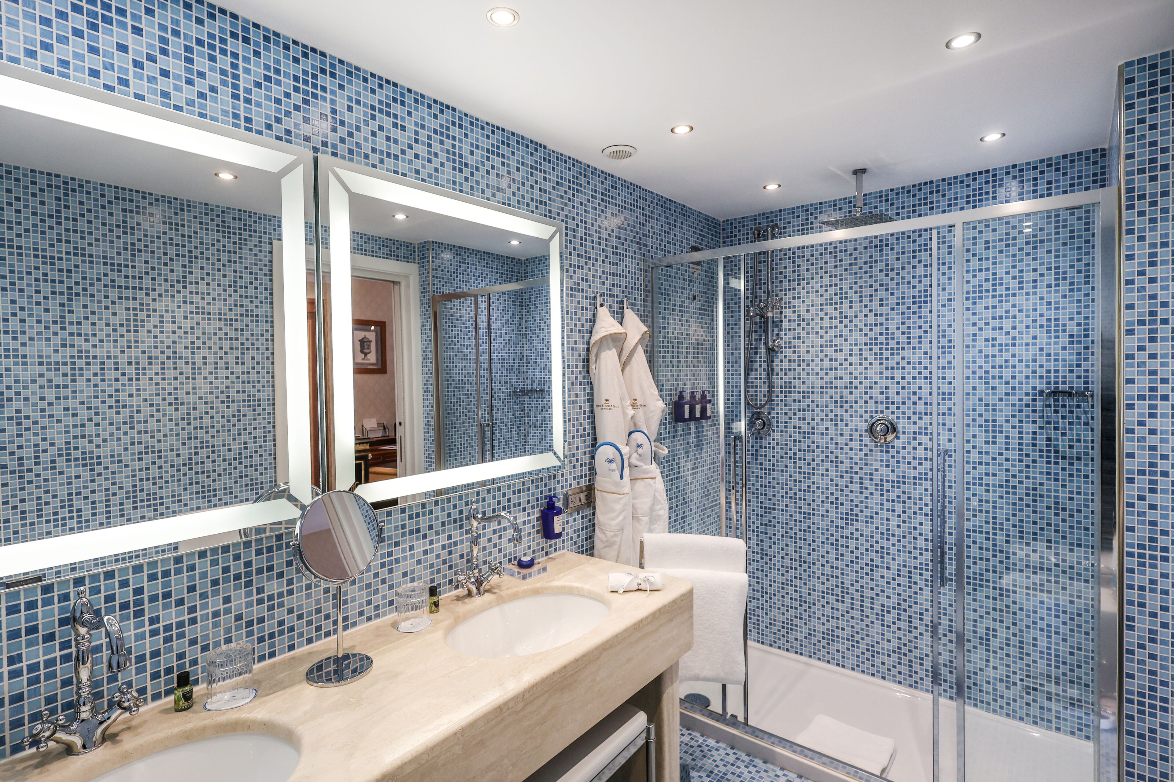 Une salle de bain avec un grand miroir, deux lavabos, une douche et des carreaux de mosaïque bleus.