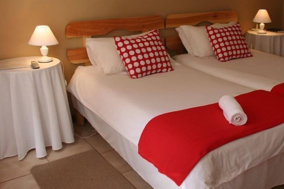 A double bed with white bedding and red accents, two bedside tables with lamps, and a red throw blanket.