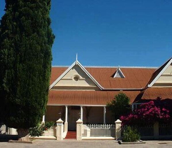 A building with a triangular roof, a central entrance with steps, and a white fence.
