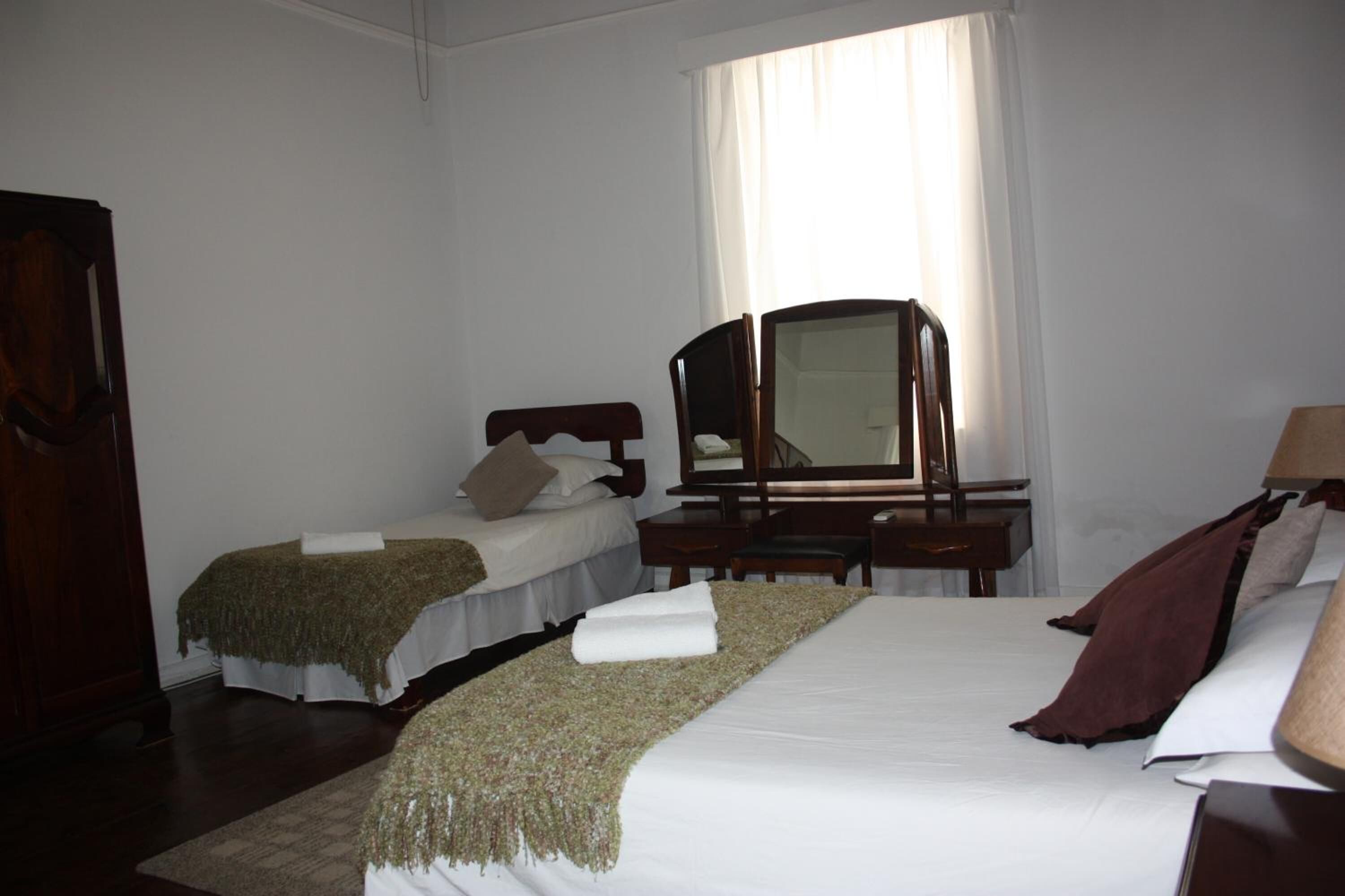 A hotel room with two beds, a desk, a mirror, and a wardrobe.