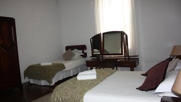 A hotel room with two beds, a desk, a mirror, and a wardrobe.