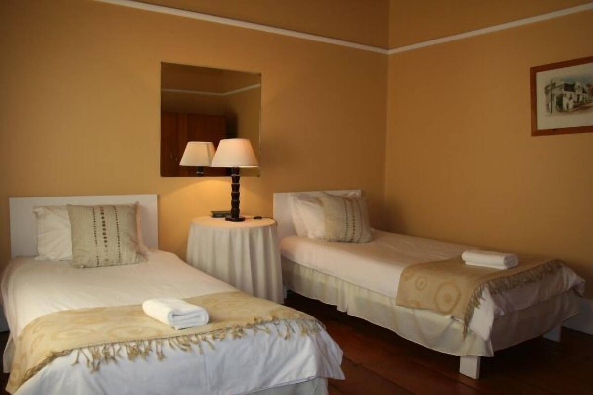 A hotel room with two single beds, a round table with a lamp, and a mirror on the wall.