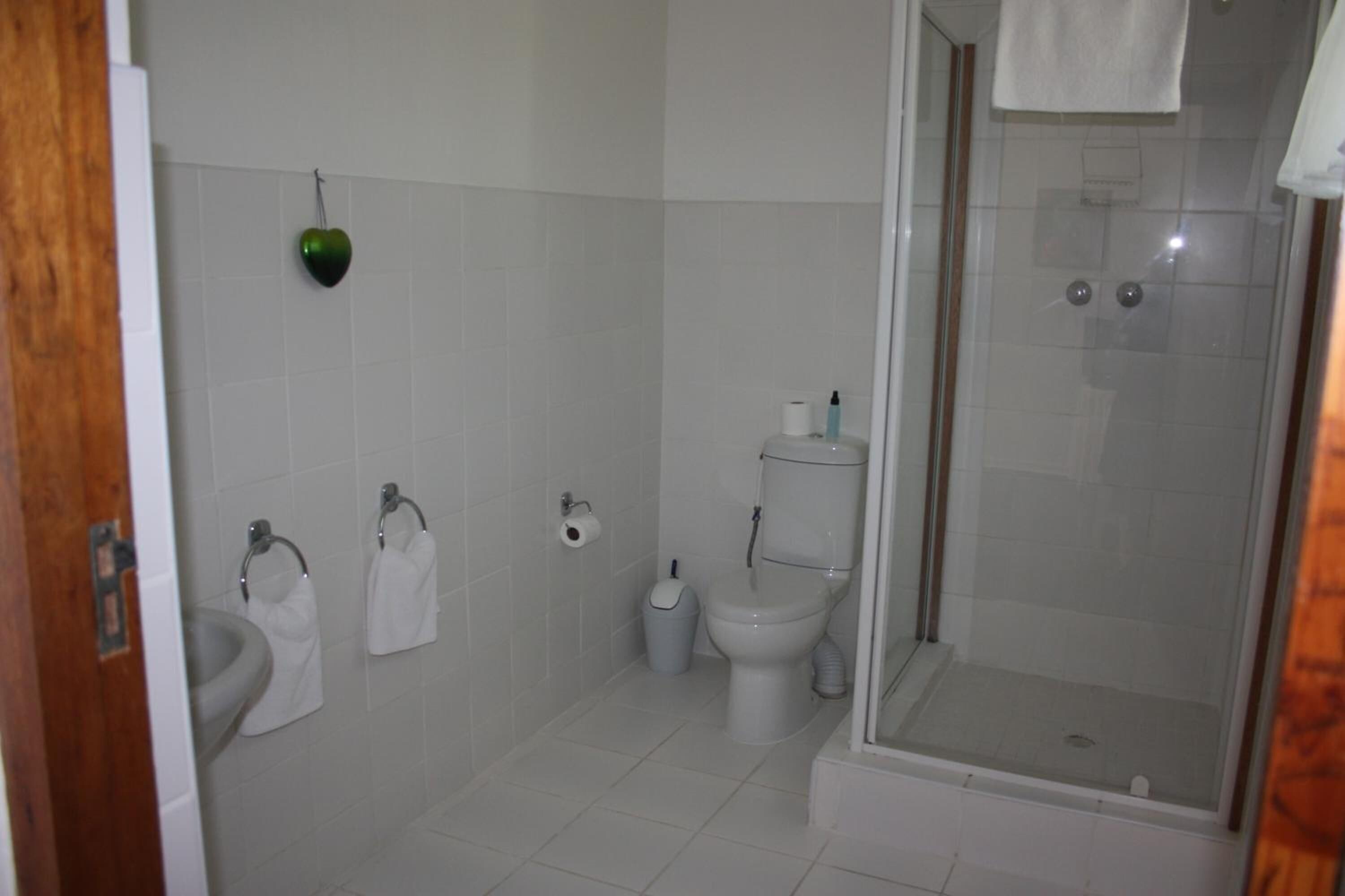 Un baño con inodoro, bidé y lavamanos, cabina de ducha de vidrio y una decoración con forma de corazón en la pared.