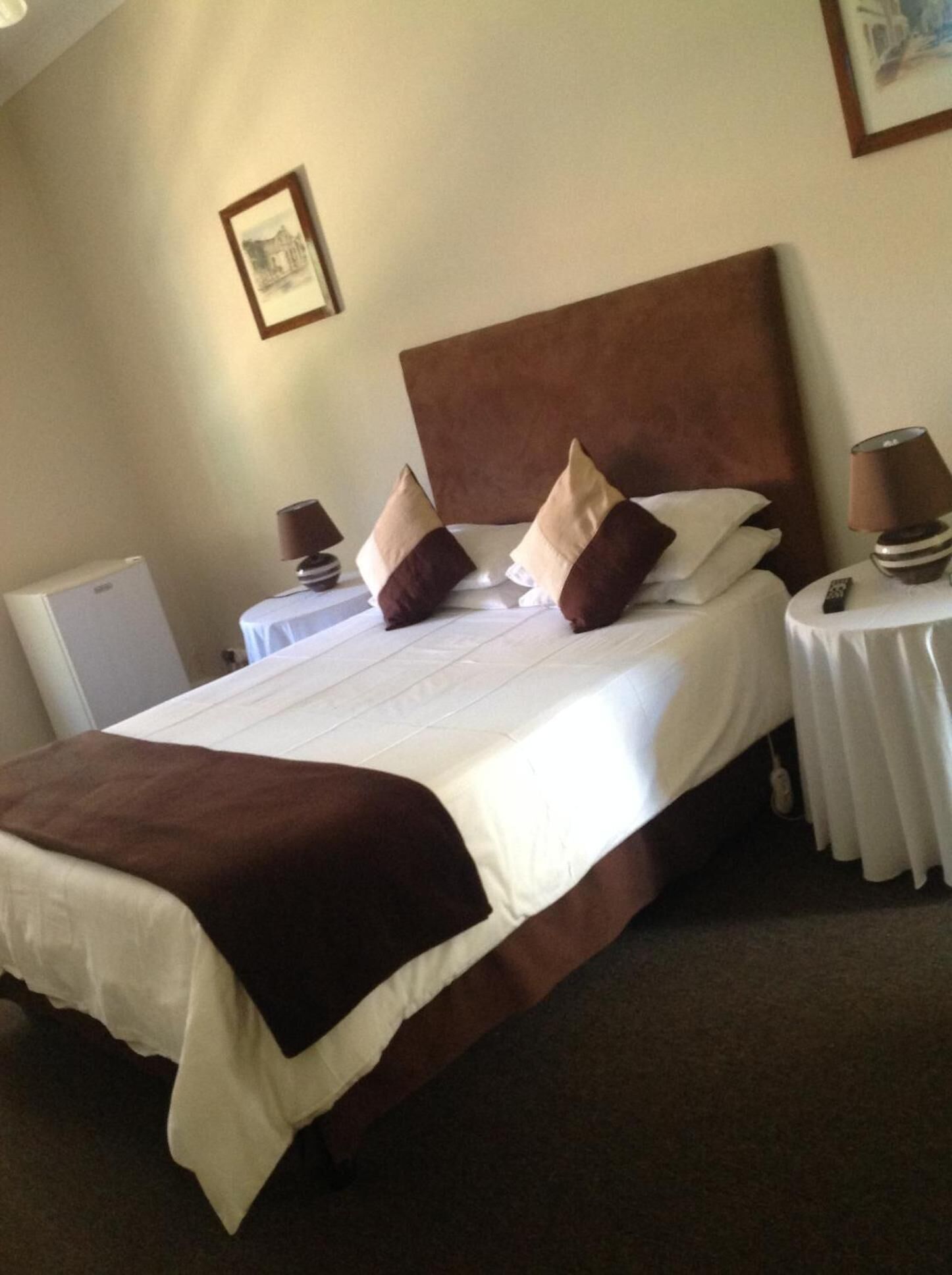 A neatly made bed with a brown headboard, white bedding, and two bedside tables with lamps.