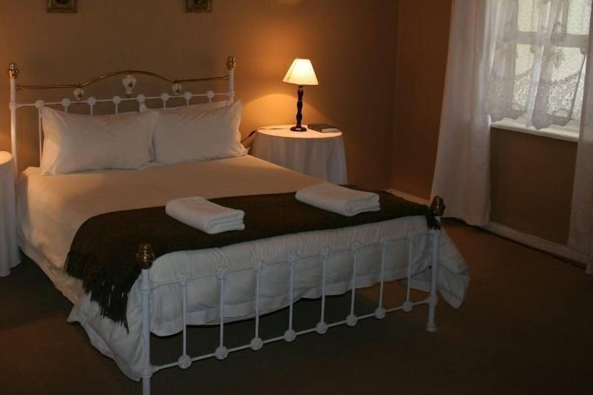 A neatly made bed with white linens, two bedside tables with lamps, and a window with sheer curtains.