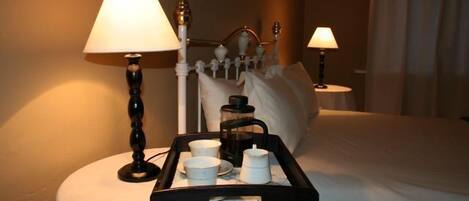 A hotel room with a bed, a bedside table with a lamp, and a tray with cups and a coffee pot.