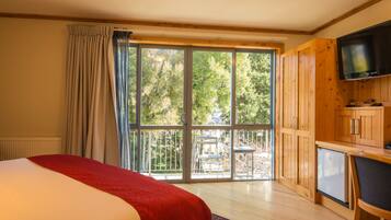 A bedroom with a large window, a bed, a TV, and a small kitchenette.
