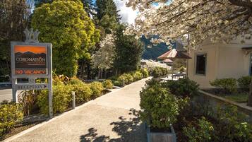 A sign for Coronation Lodge with a "No Vacancy" message, a reception area, and a pathway leading to a building surrounded by trees and a mountain backdrop.