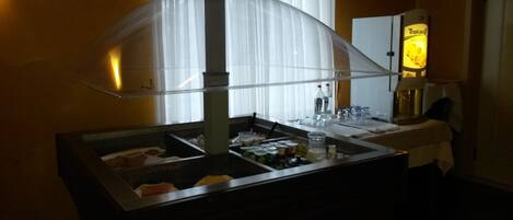 A buffet setup with a glass enclosure, food items, and a refrigerator in the background.