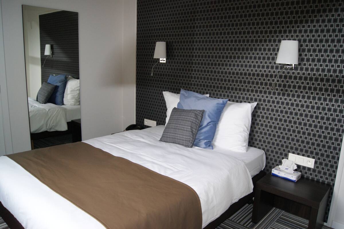 Habitación de hotel con una cama grande, una mesita de noche, un espejo y azulejos con diseño en la pared.