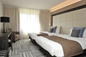 A hotel room with two beds, a desk, a chair, and a large window with curtains. - Malpertuus (Riemst)