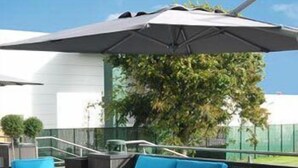 An outdoor seating area with a table and chairs, a large umbrella, and a staircase leading to a building. - Malpertuus (Riemst)