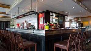 A modern bar area with a long counter, multiple stools, and a variety of bottles and glasses. - Malpertuus (Riemst)