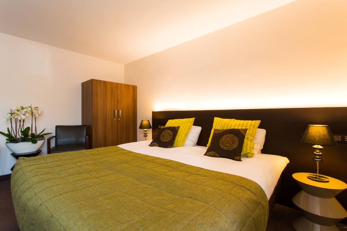 Habitación de hotel con una cama grande, un armario de madera, un escritorio y una planta en maceta.