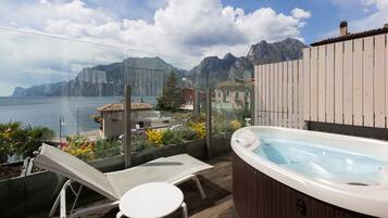 A balcony with a hot tub, lounge chairs, and a view of the sea and mountains.