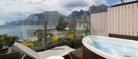 Een balkon met een jacuzzi, lounge stoelen en uitzicht op zee en bergen.