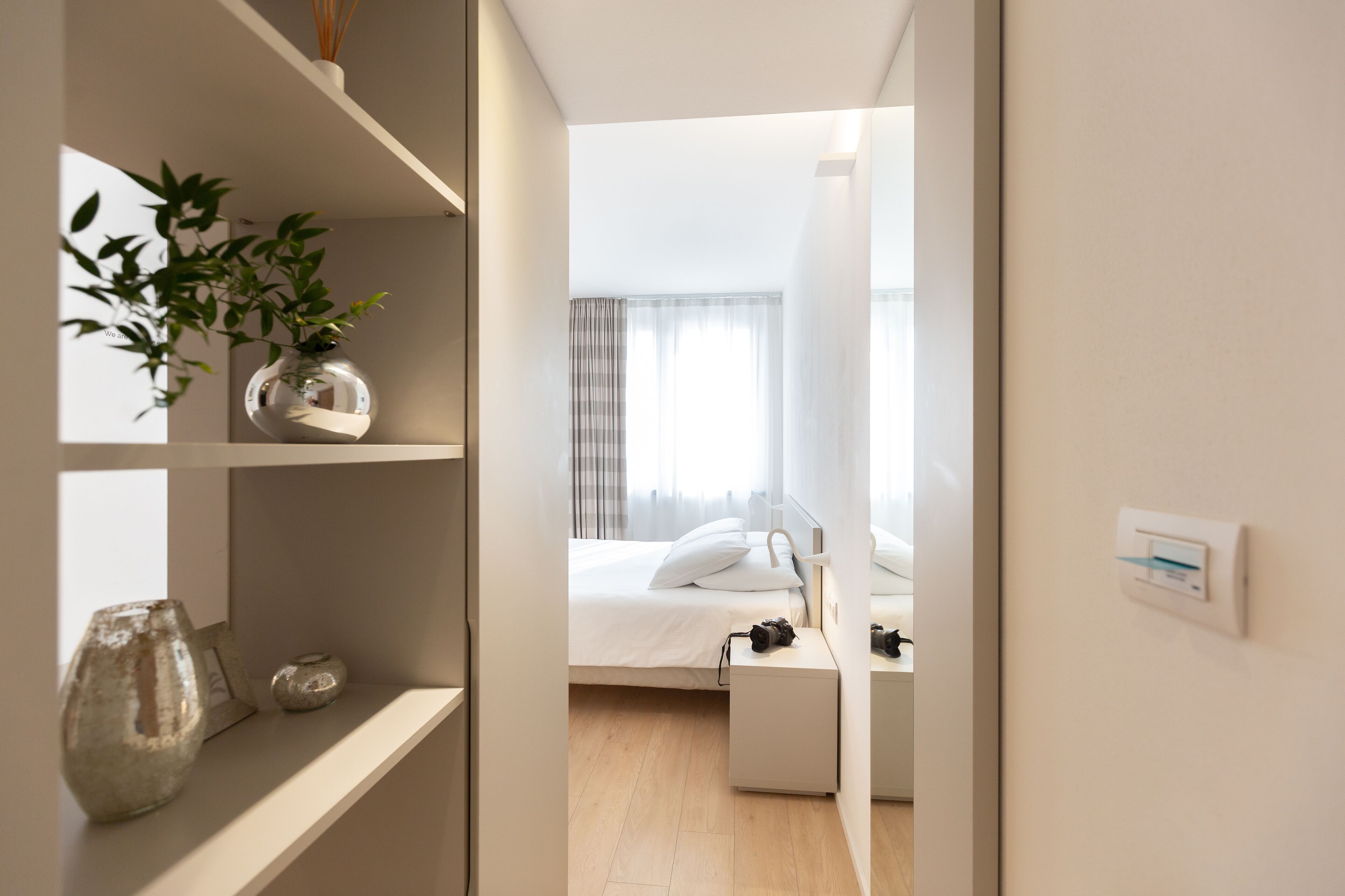 A modern hotel room with a bed, bedside table, and a small plant on a shelf.