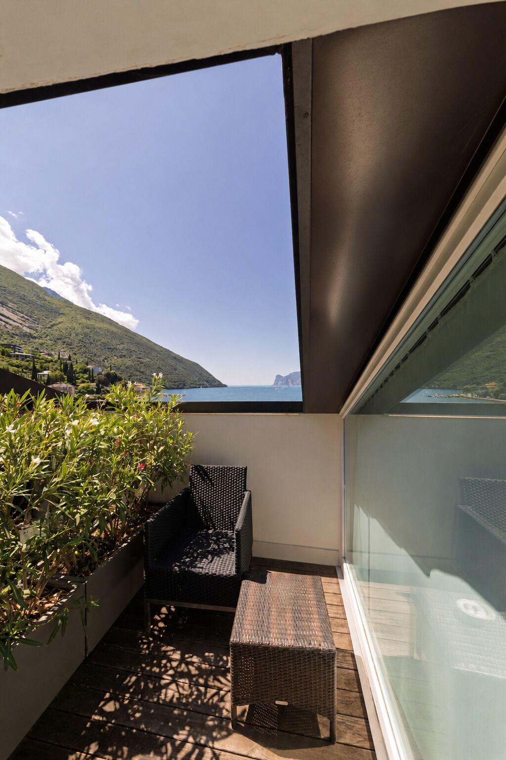 Een balkon met een rieten stoel en tafel, een potplant en uitzicht op een berg en de zee.