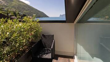 Un balcone con una sedia e un tavolino in vimini, una pianta in vaso e vista su montagna e mare.