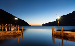 A calm waterfront at dusk with a pier extending into the water, surrounded by mountains. - Hotel Lago di Garda (Nago-Torbole)