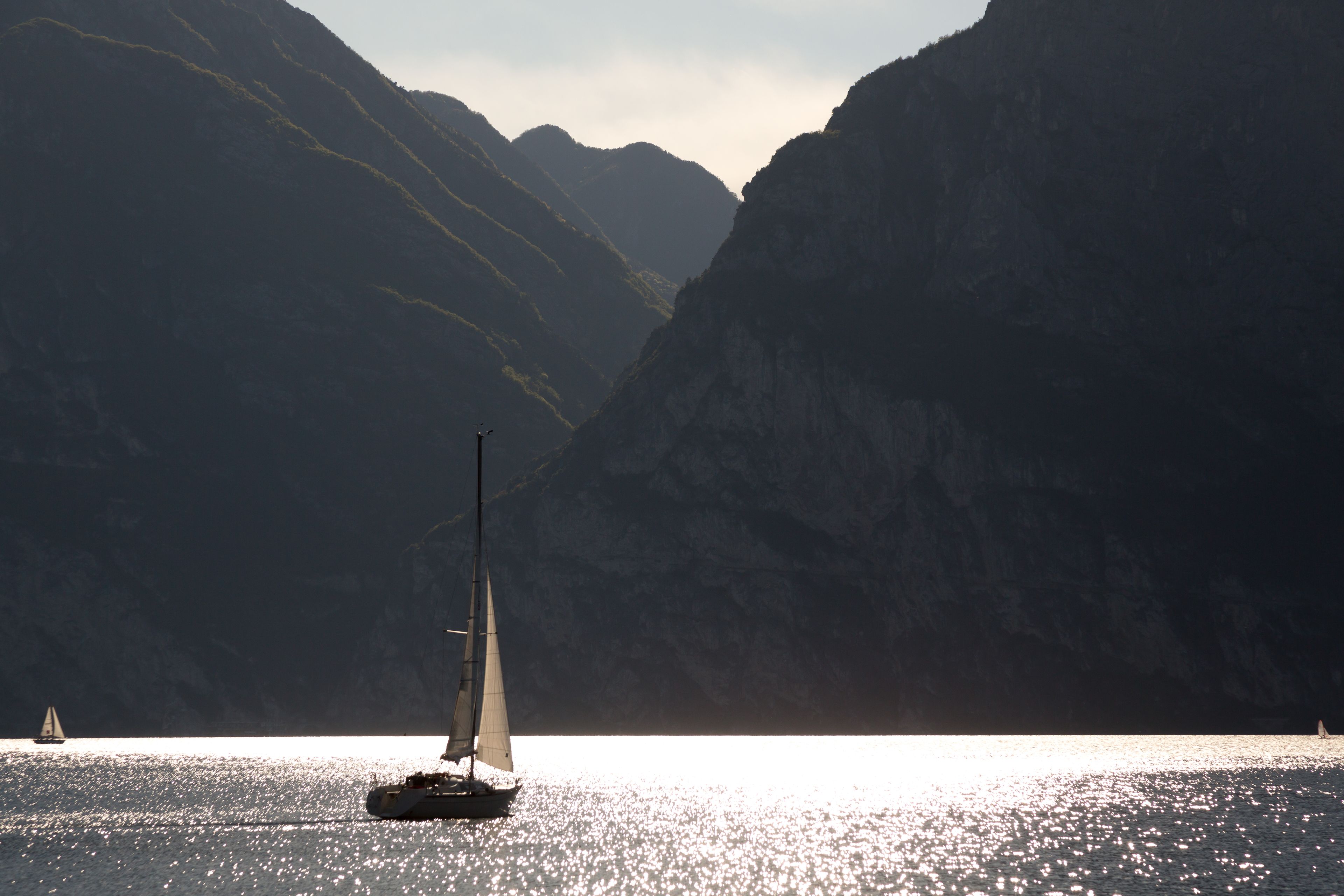 A sailboat on calm water with mountainous terrain in the background.
