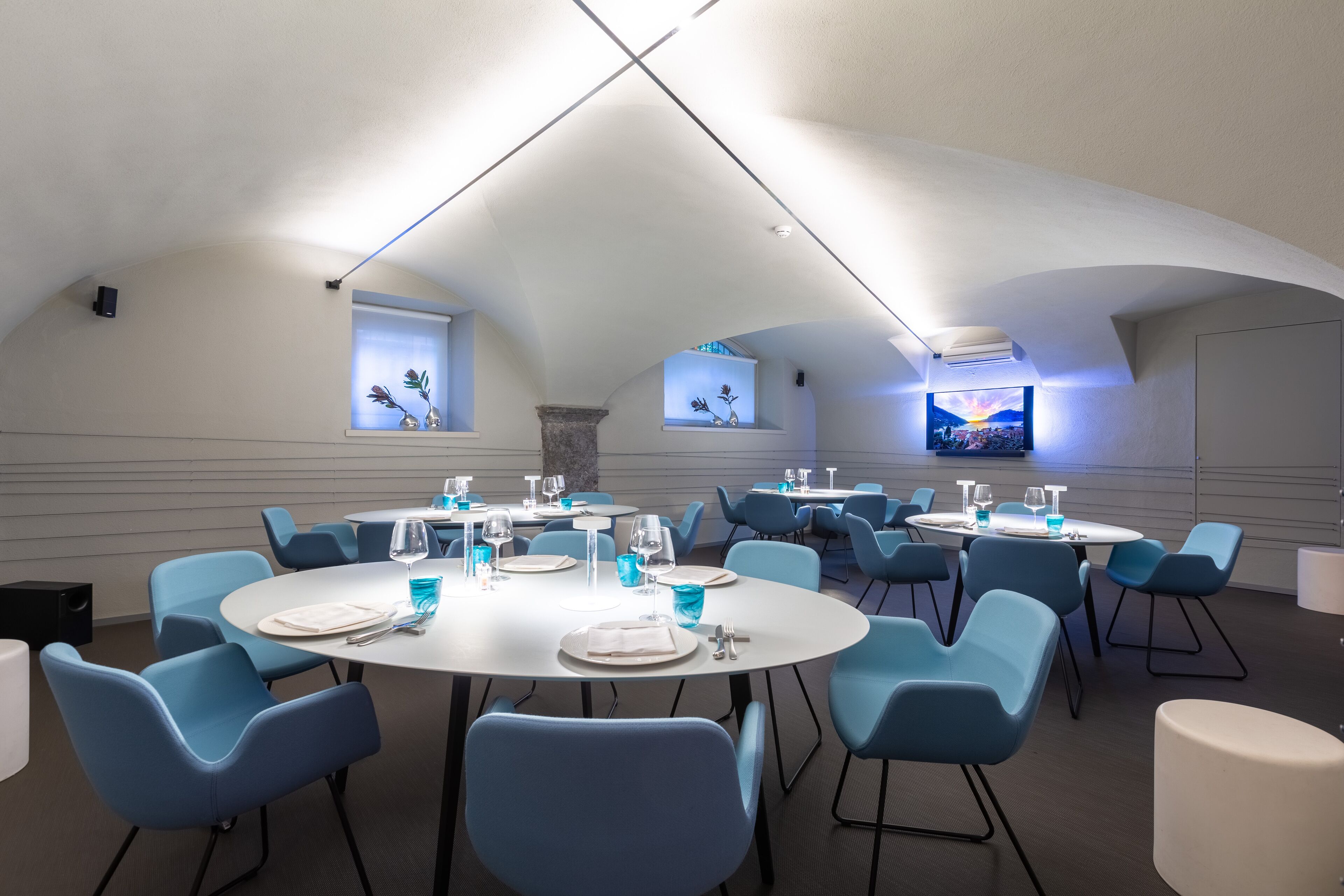 A dining area with round tables and blue chairs, featuring a modern ceiling design and decorative wall elements.