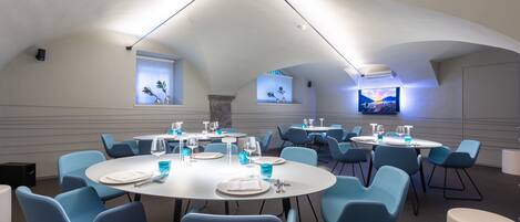 A dining area with round tables and blue chairs, featuring a modern ceiling design and decorative wall elements.