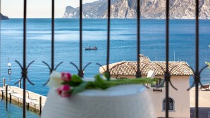 A coastal view with a clear sky, a boat on the water, and a building with a tiled roof. - Hotel Lago di Garda (Nago-Torbole)