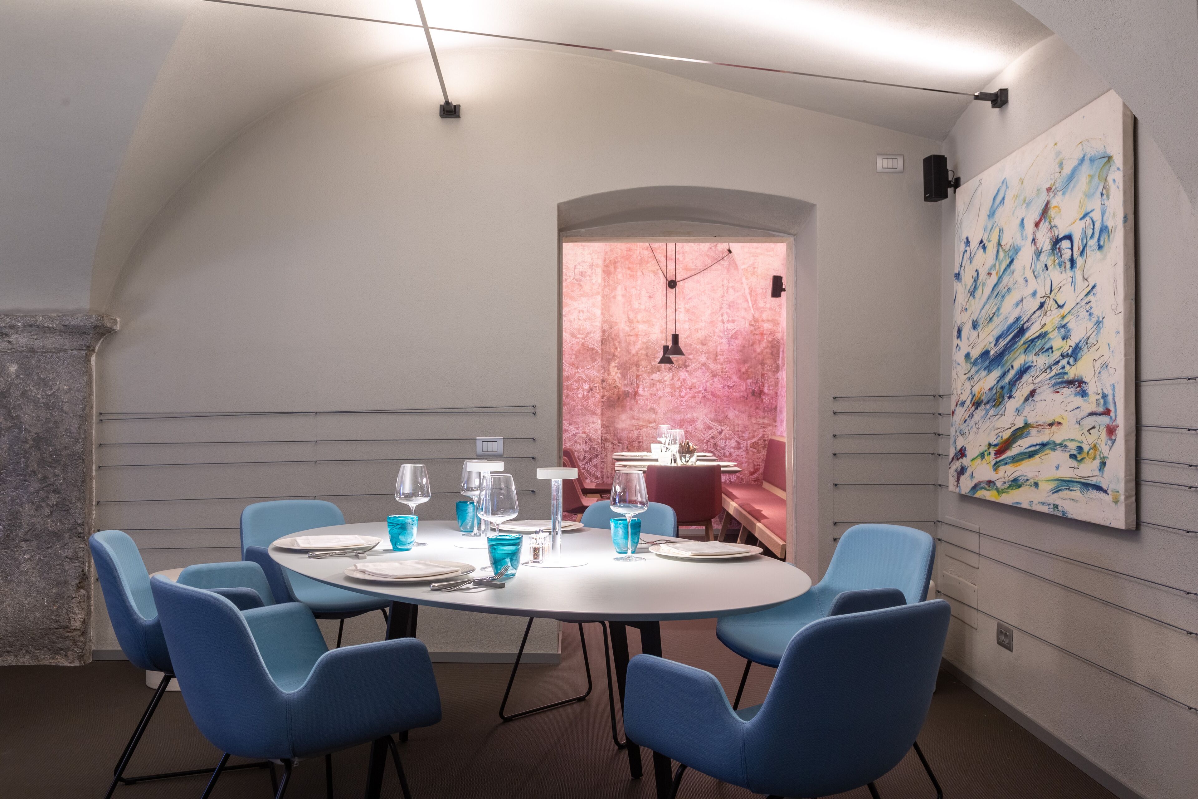 Une salle de conférence avec une table ronde, des chaises bleues et un grand tableau abstrait accroché au mur.