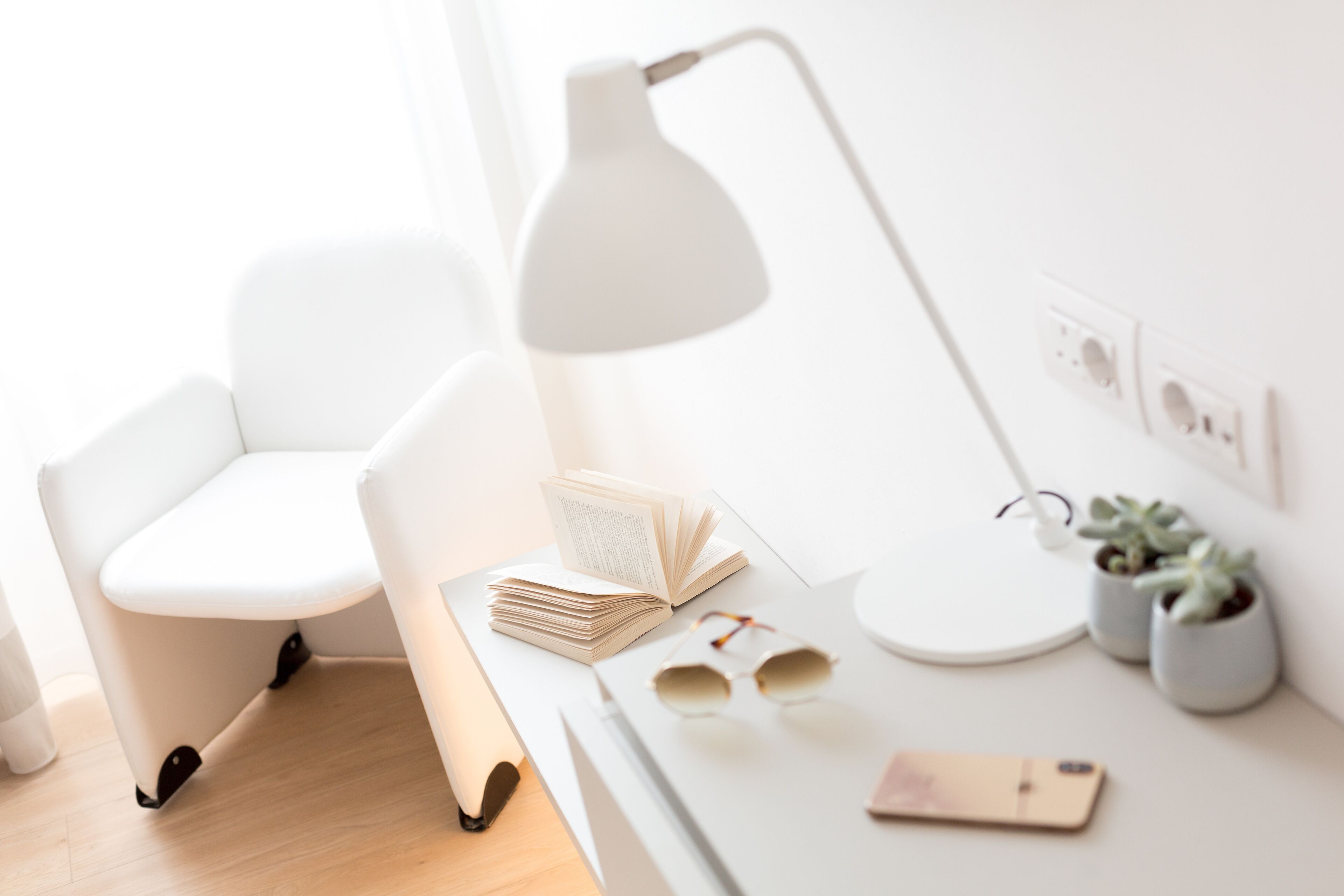 A modern, minimalist workspace with a white chair, desk, and lamp.
