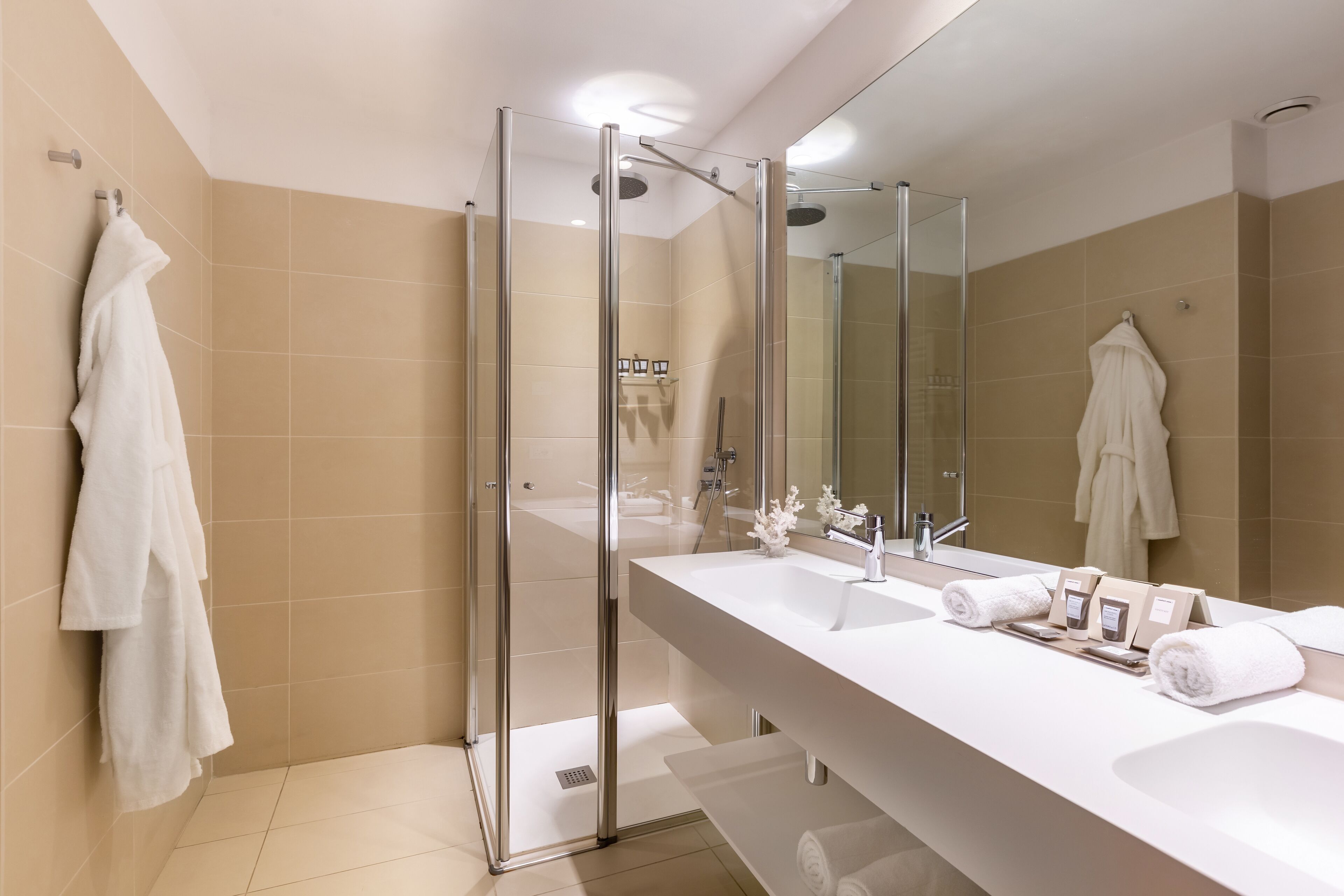 A modern bathroom with a glass-enclosed shower, a large mirror, and a white vanity with multiple sinks and towels.