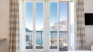 A hotel room with a bed, a TV, and a balcony with a view of the sea and mountains. - Hotel Lago di Garda (Nago-Torbole)