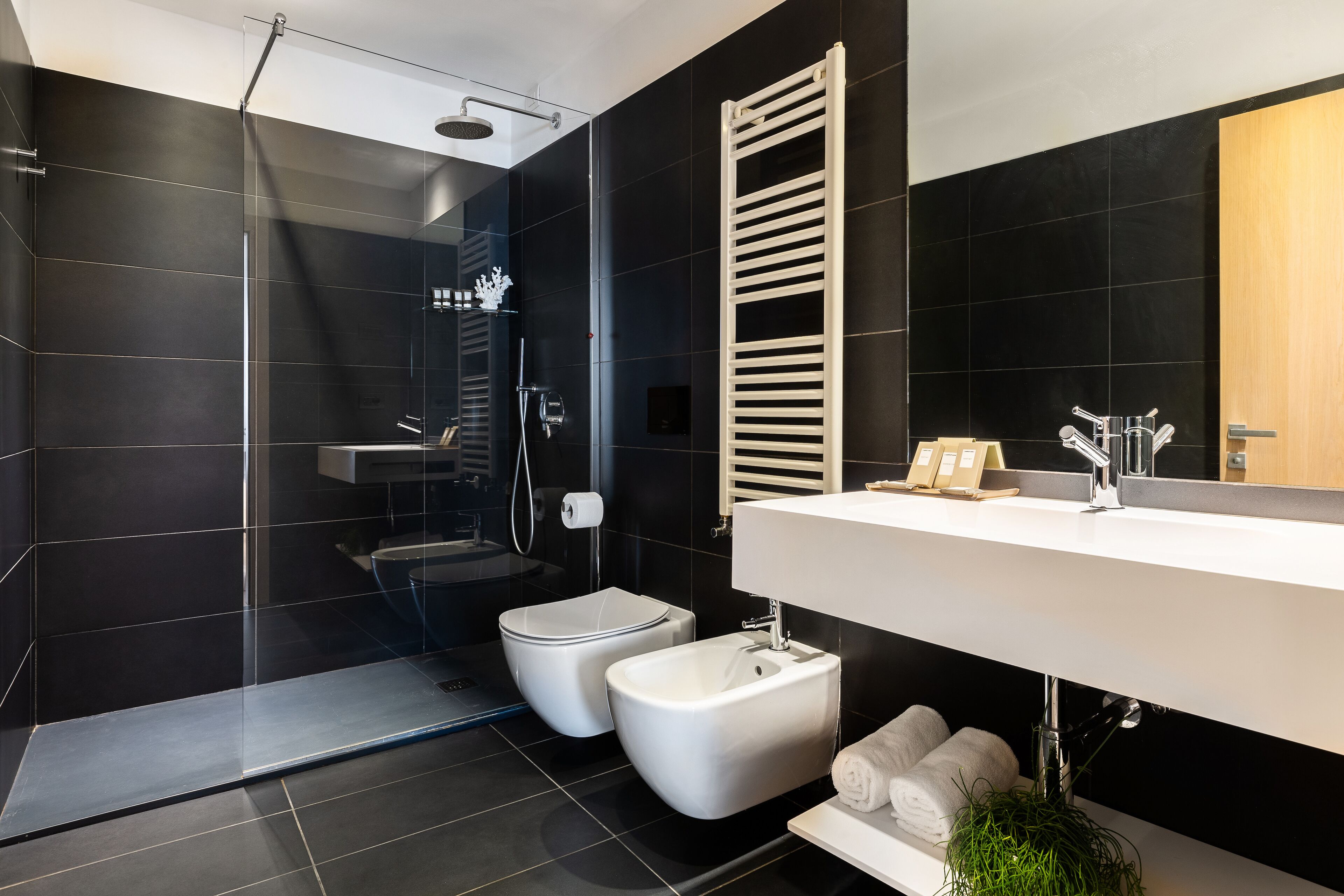Un baño moderno con ducha envuelta en vidrio, inodoro blanco, bidet y un espejo grande sobre un lavabo blanco.