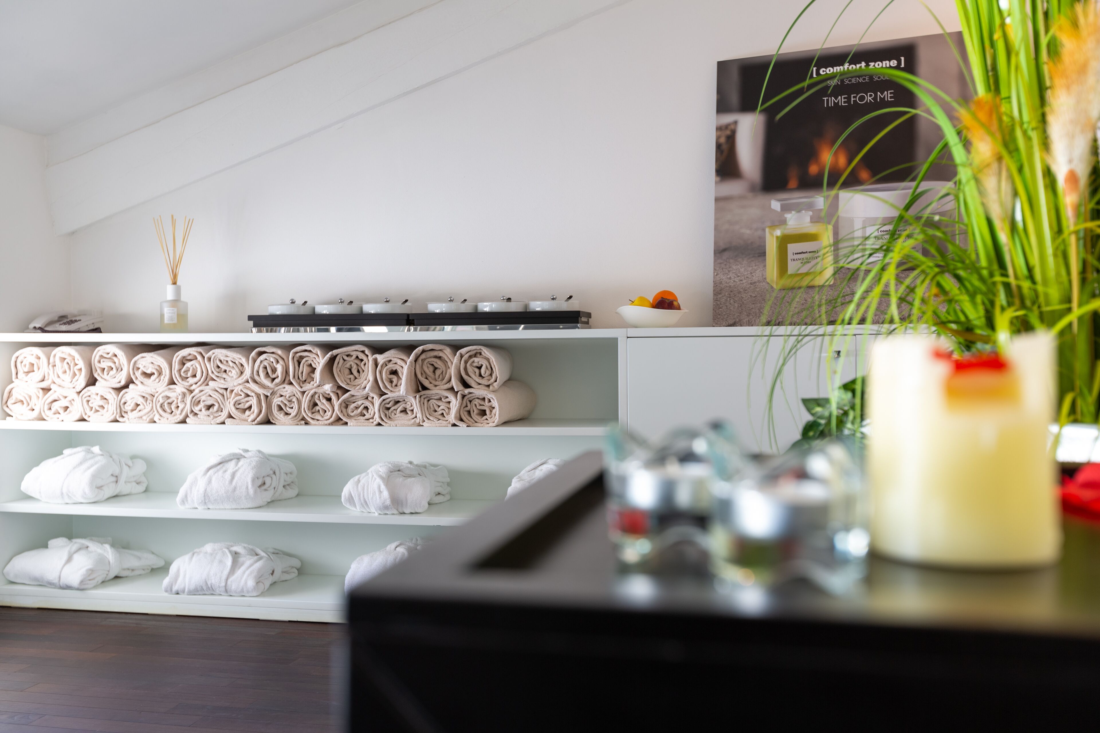 Quarto de hotel com toalhas bem dobradas nas prateleiras, um minibar e uma televisão na parede exibindo um anúncio de conforto.