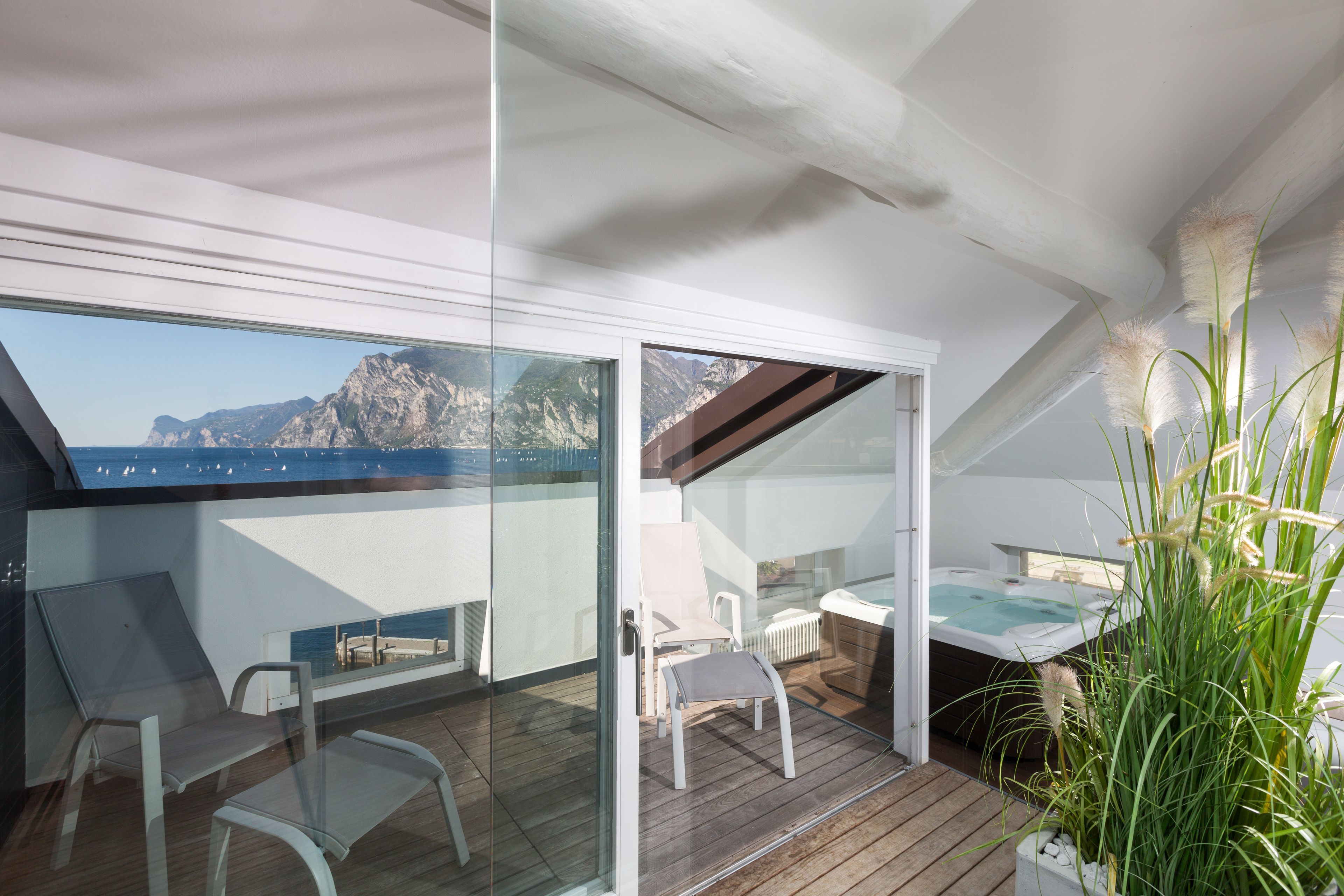 A balcony with a glass door, a hot tub, and a view of the sea.