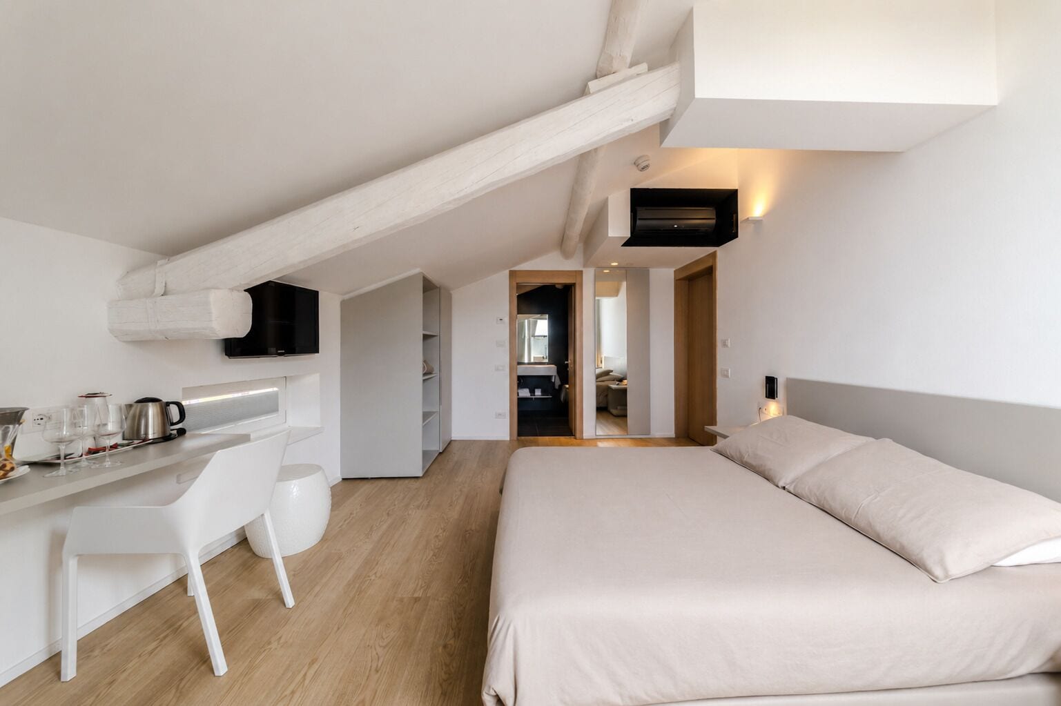 Una habitación de hotel moderna con cama, un escritorio y silla, una kitchenette y un baño visible a través de una puerta abierta.