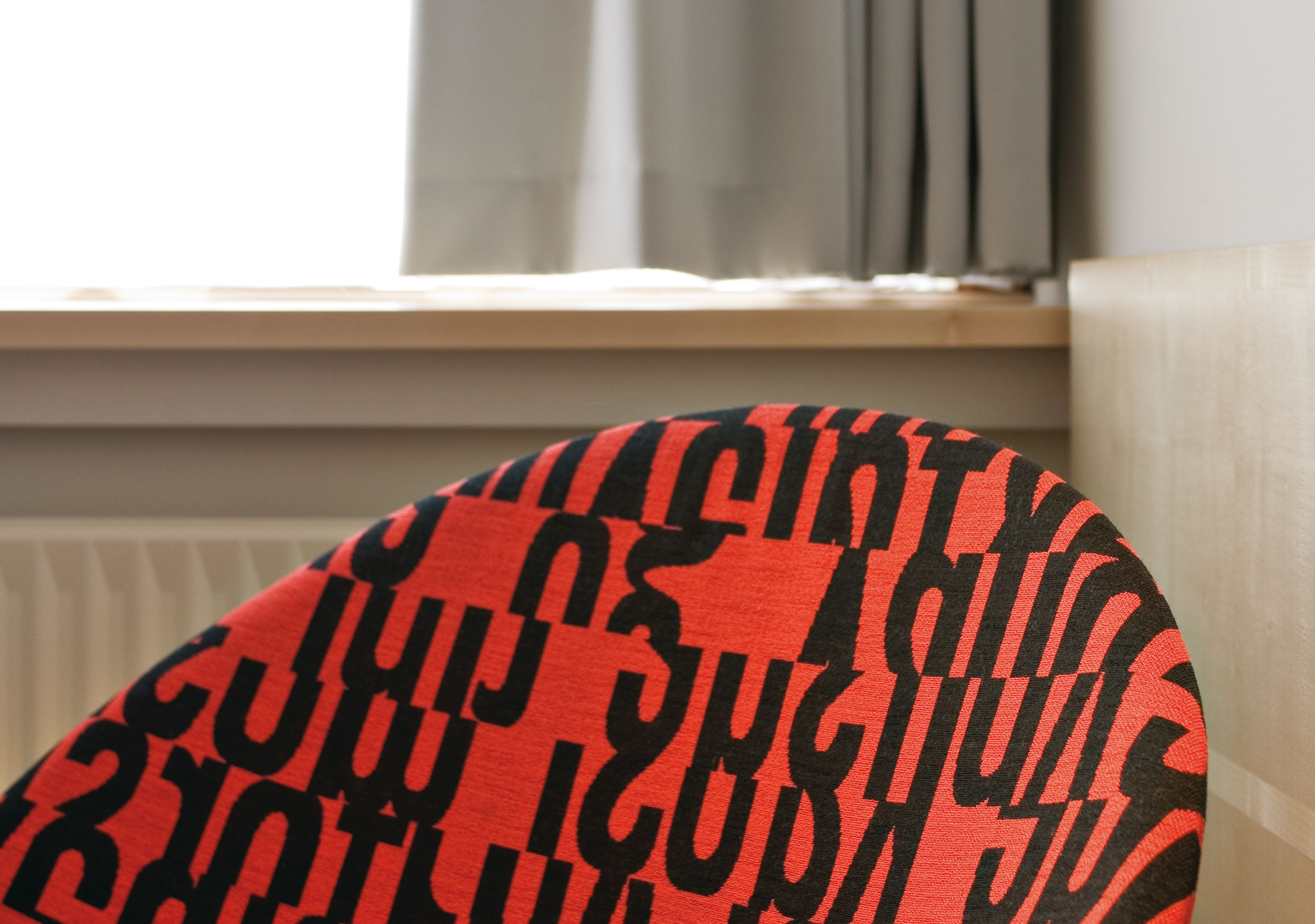 A close-up of a red and black patterned pillow against a wall.