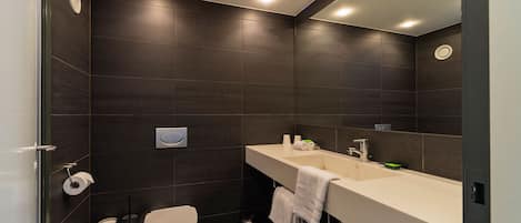 Un baño moderno con baldosas oscuras, un inodoro, un lavabo con espejo y un cubo de basura.