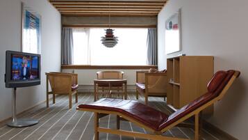 Una habitación con televisor, una butaca reclinable, dos sillas, un armario de madera y una ventana con cortinas.