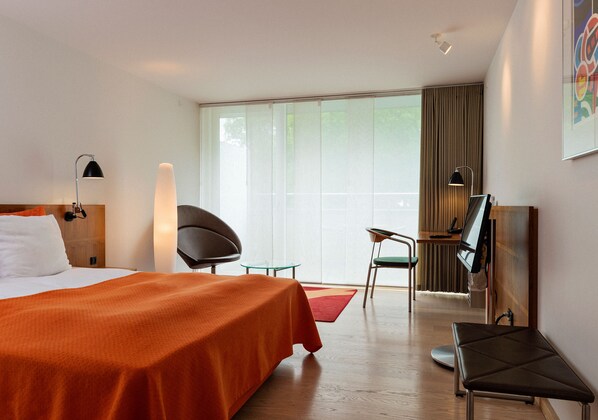A hotel room with a bed, a desk, a chair, a TV, and a large window. - Konventum Konferencecenter (Helsingor)